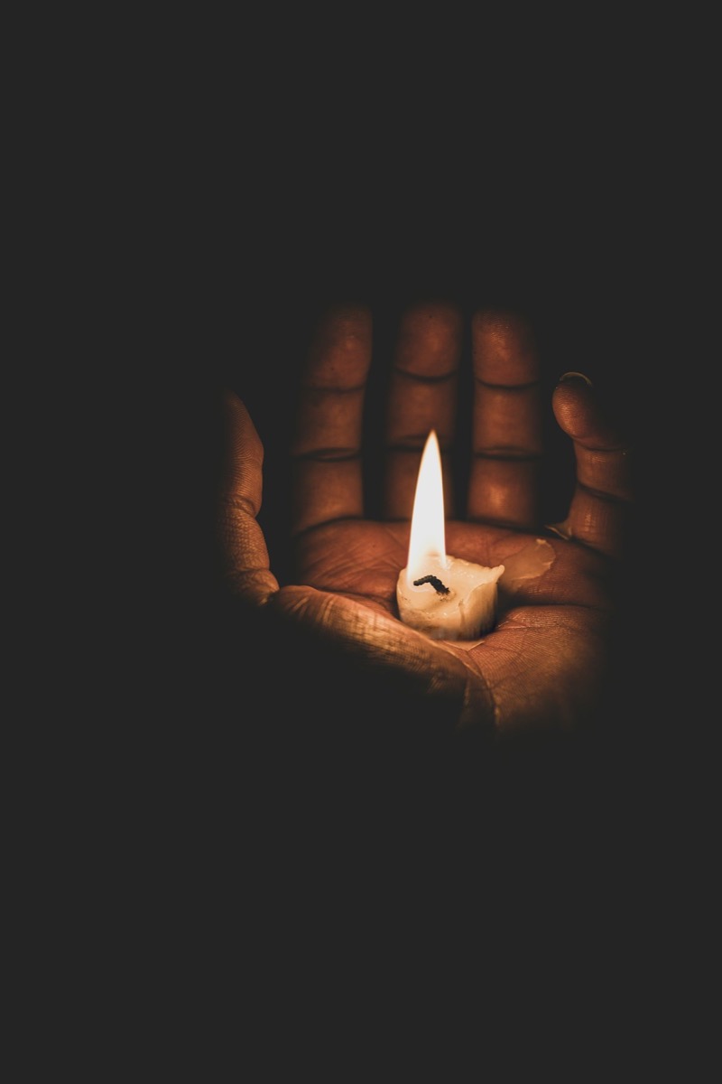 Two hands holding a lit candle in the dark